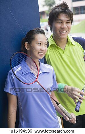 Stock Photograph - Close-up of a young couple holding badminton rackets and smiling. Fotosearch