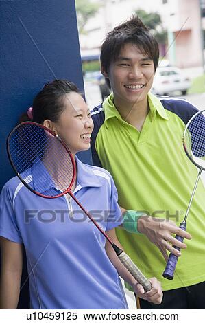 Stock Photography - Close-up of a young couple holding badminton rackets and smiling. Fotosearch