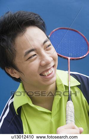 Stock Image - Close-up of a young man holding a badminton racket and smiling. Fotosearch