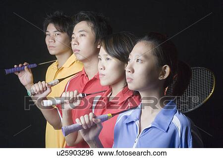 Stock Photograph - Close-up of two young women and two young men standing side by side with badminton rackets. Fotosearch