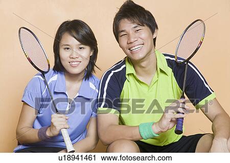 Stock Image - Portrait of a young couple holding badminton rackets and smiling. Fotosearch