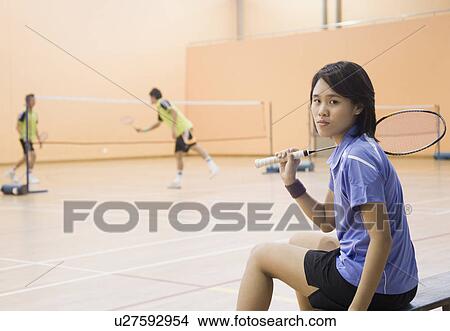 Portrait of a young woman sitting on a bench and holding a badminton racket View Large Photo Image Picture - Portrait of a young woman sitting on a bench and holding a badminton racket. Fotosearch