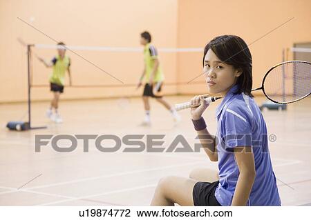 Stock Image - Portrait of a young woman sitting on a bench and holding a badminton racket. Fotosearch