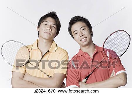 Stock Image - Portrait of two young men holding badminton rackets and smiling. Fotosearch