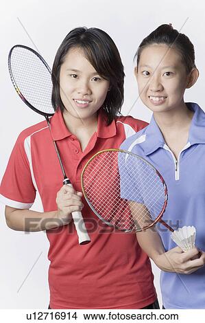 Picture - Portrait of two young women holding badminton rackets and smiling. Fotosearch