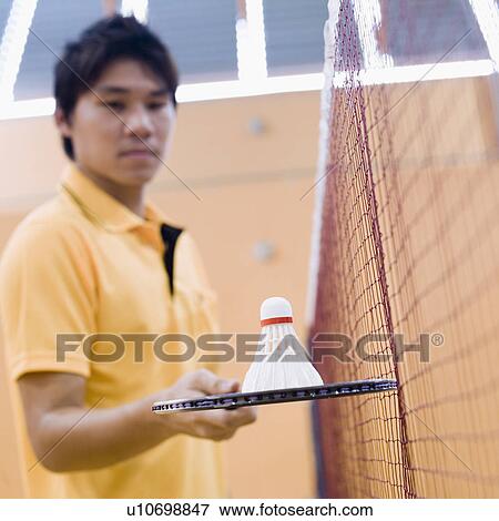 Stock Photo - Side profile of a young man standing in a badminton court and holding a badminton racket. Fotosearch