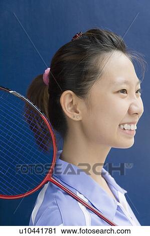 Stock Image - Side profile of a young woman with a badminton racket and smiling. Fotosearch