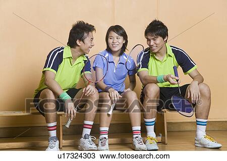 Two young men and a young woman sitting side by side on a bench and holding badminton rackets View Large Photo Image Stock Image - Two young men and a young woman sitting side by side on a bench and holding badminton rackets. Fotosearch