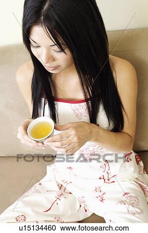 Stock Image - Close-up of a young woman holding a cup of herbal tea. Fotosearch