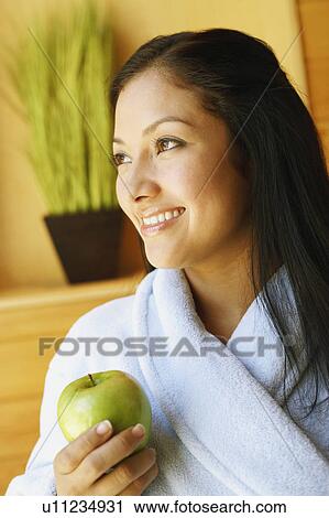 Stock Image - Close-up of a young woman holding an apple and smiling. Fotosearch