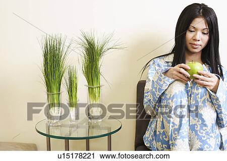 Stock Image - Close-up of a young woman sitting and holding a green apple. Fotosearch