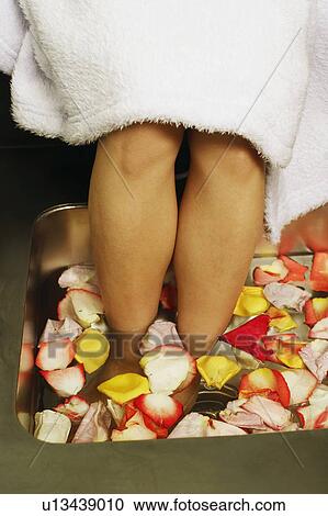 Stock Image - Low section view of a woman's feet soaked in a tub of flower petals and water. Fotosearch