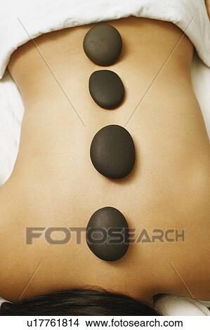 Picture - Mid section view of a woman getting hot stone therapy. Fotosearch