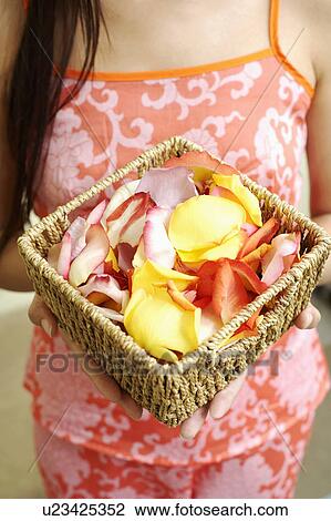 Stock Image - Mid section view of a woman holding a basket of flower petals. Fotosearch