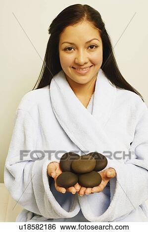 Stock Photograph - Portrait of a young woman holding spa hot stones and smiling. Fotosearch
