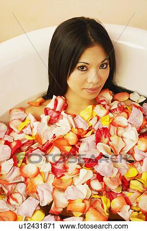 Stock Image - Portrait of a young woman in a bathtub filled with flower petals. Fotosearch