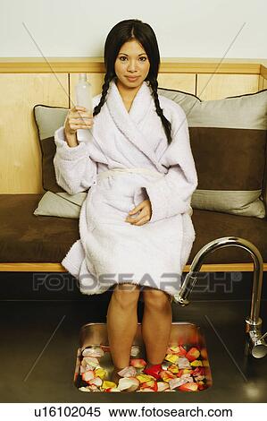Stock Photography - Portrait of a young woman with her feet soaked in a tub of water and flower petals. Fotosearch