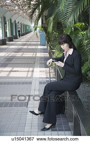 Businesswoman sitting on a railing and using a mobile phone View Large Photo Image Stock Photo - Businesswoman sitting on a railing and using a mobile phone. Fotosearch