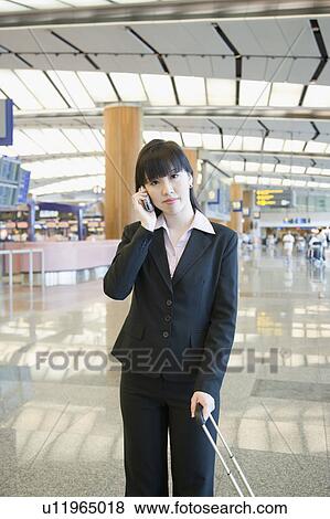 Stock Photo - Businesswoman talking on a mobile phone at an airport lounge. Fotosearch