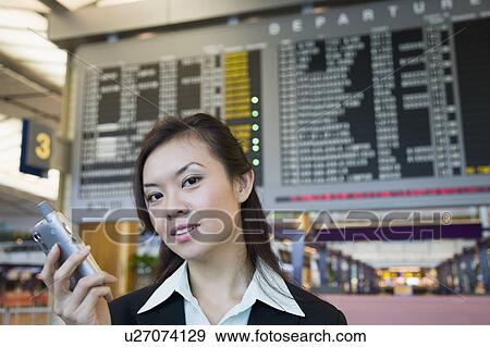 Stock Photo - Close-up of a businesswoman at an airport holding a mobile phone. Fotosearch