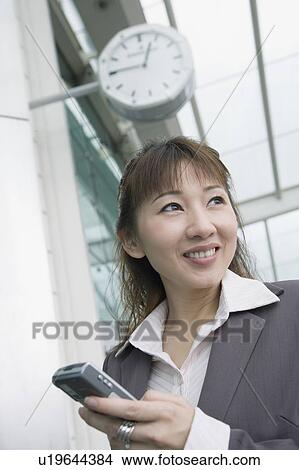 Low angle view of a businesswoman holding a mobile phone and waiting at an airport lounge View Large Photo Image Picture - Low angle view of a businesswoman holding a mobile phone and waiting at an airport lounge. Fotosearch