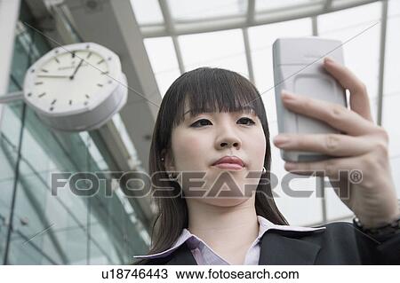 Stock Image - Low angle view of a businesswoman using a personal data assistant and waiting at an airport lounge. Fotosearch