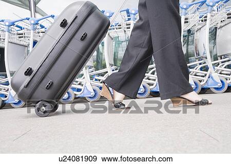 Stock Photo - Low section view of a businesswoman pulling luggage outside an airport. Fotosearch