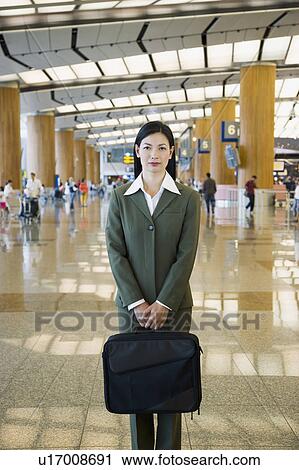 Stock Image - Portrait of a businesswoman standing at an airport lounge with a bag. Fotosearch