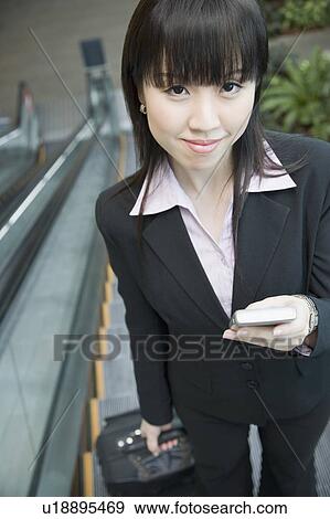 Stock Photo - Portrait of a businesswoman standing on an escalator and holding a mobile phone. Fotosearch
