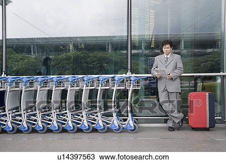 Stock Image - Businessman reading a document and waiting outside an airport. Fotosearch