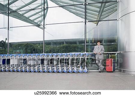 Stock Photograph - Businessman reading a document and waiting outside an airport. Fotosearch