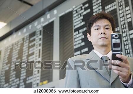 Close-up of a businessman at an airport holding a mobile phone View Large Photo Image Stock Photography - Close-up of a businessman at an airport holding a mobile phone. Fotosearch
