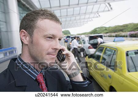 Picture - Close-up of a businessman talking on a mobile phone outside an airport. Fotosearch