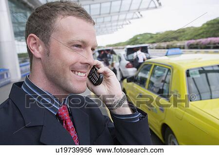 Stock Photograph - Close-up of a businessman talking on a mobile phone outside an airport. Fotosearch