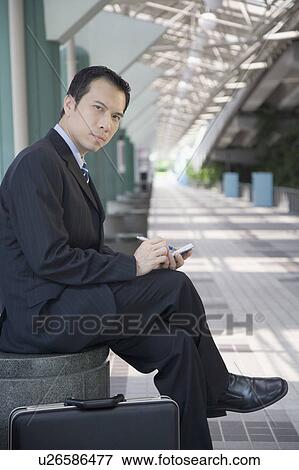 Stock Photo - Portrait of a businessman sitting and using a palmtop. Fotosearch