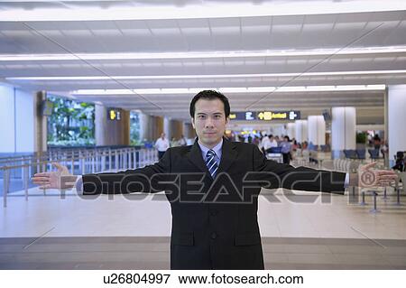 Stock Photo - Portrait of a businessman standing in a airport lounge with his arms outstretched. Fotosearch