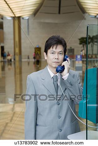 Stock Image - Portrait of a businessman using a pay phone. Fotosearch