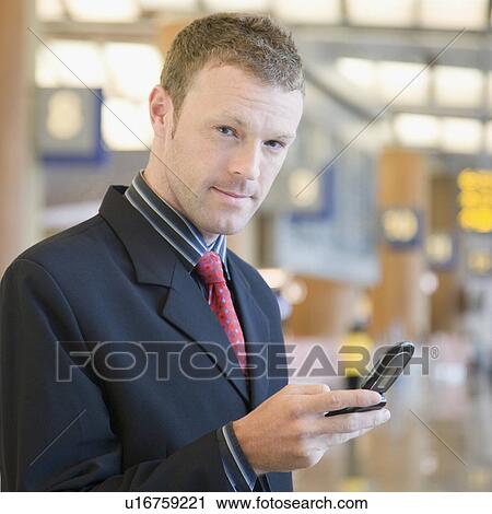 Stock Image - Portrait of a businessman using a mobile phone at an airport lounge. Fotosearch