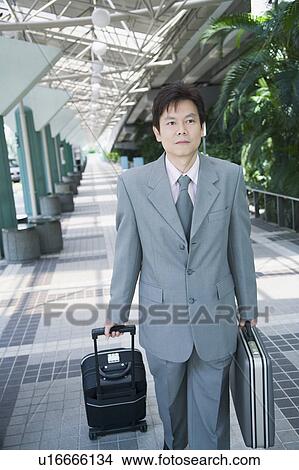 Picture - Portrait of a businessman walking with his luggage and suitcase. Fotosearch