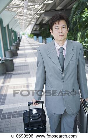 Stock Photograph - Portrait of a businessman walking with his luggage and suitcase. Fotosearch