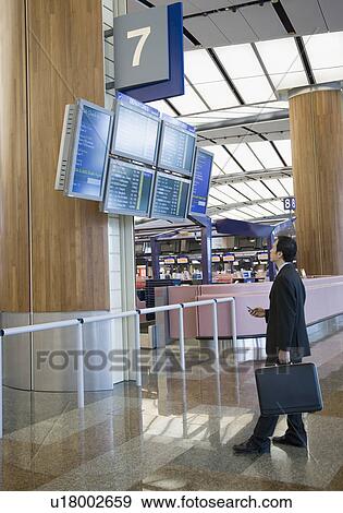 Side profile of a businessman looking at an arrival departure board at an airport View Large Photo Image Stock Photo - Side profile of a businessman looking at an arrival departure board at an airport. Fotosearch