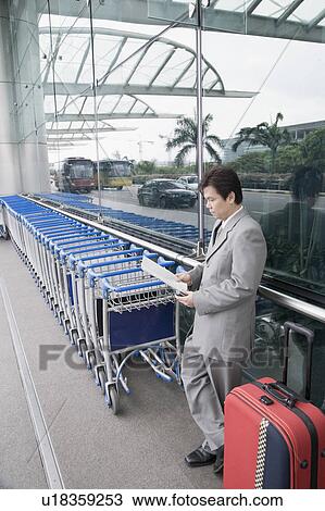 Stock Image - Side profile of a businessman reading a document and waiting outside an airport. Fotosearch