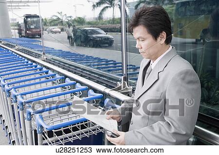 Stock Image - Side profile of a businessman reading a document and waiting outside an airport. Fotosearch