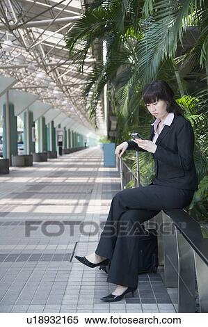 Businesswoman sitting on a railing and using a mobile phone View Large Photo Image Stock Photography - Businesswoman sitting on a railing and using a mobile phone. Fotosearch