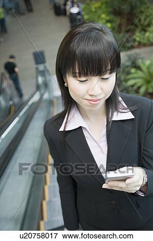 Stock Photo - Businesswoman standing on an escalator and looking at a mobile phone. Fotosearch
