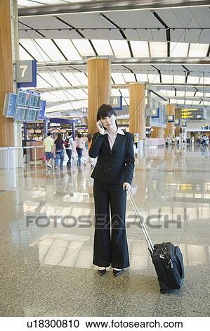 Stock Image - Businesswoman talking on a mobile phone at an airport lounge. Fotosearch