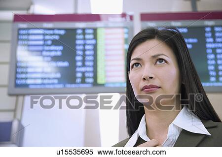 Stock Photography - Low angle view of a businesswoman in front of an arrival departure board. Fotosearch
