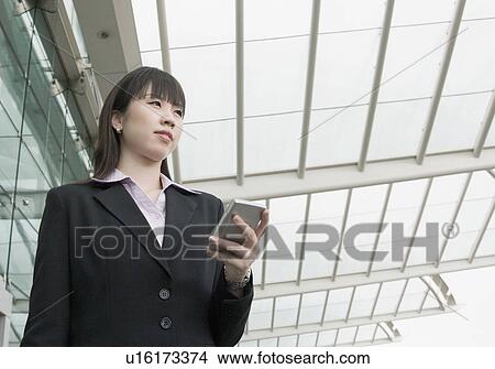 Picture - Low angle view of a businesswoman holding a personal data assistant and waiting at an airport lounge. Fotosearch