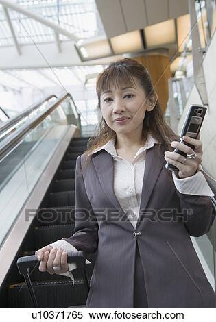 Stock Photography - Portrait of a businesswoman holding a mobile phone and a suitcase. Fotosearch