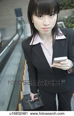 Portrait of a businesswoman standing on an escalator and holding a mobile phone View Large Photo Image Stock Image - Portrait of a businesswoman standing on an escalator and holding a mobile phone. Fotosearch